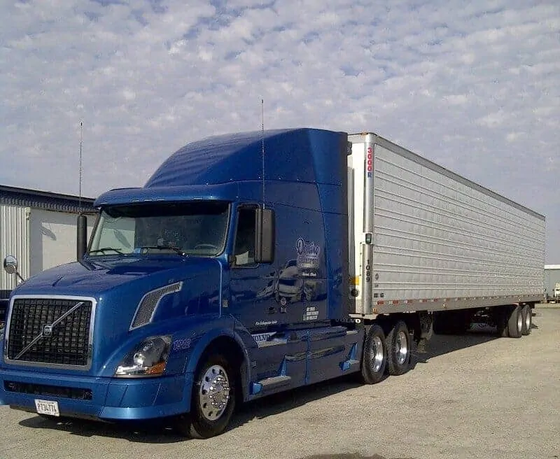 A photo of a Volvo truck in royal blue. A trailer is attached.