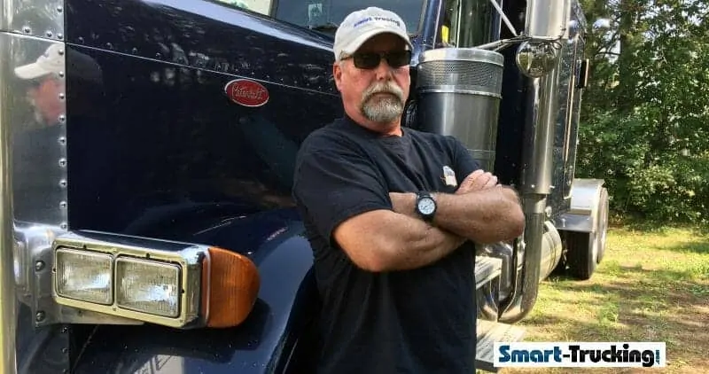 A photo of a truck driver standing beside a blue Peterbilt truck.