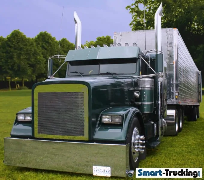 A photo of a custom long-nose truck, colored green with chrome bumper and exhaust pipes. The trailer, which is completely chrome, can be seen in the background.
