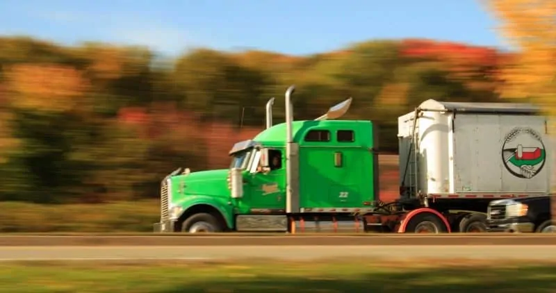 A photo of a green truck on the highway, with motion blur. 