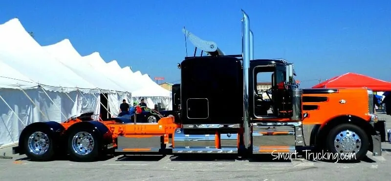 A photo of a long-nose Peterbilt 389 show truck. The truck's 'snout' is colored orange, while the body is black. There is no trailer attached.   