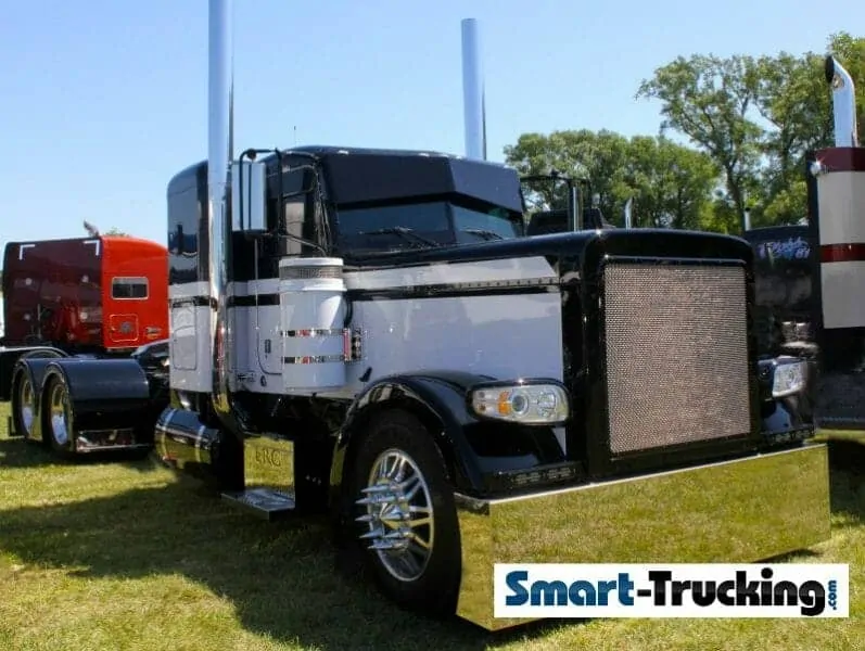 A photo of a long-nose 2009 Peterbilt 389 Glider truck, colored black with white stripes. The truck is 'bobtail', without a trailer attached. 