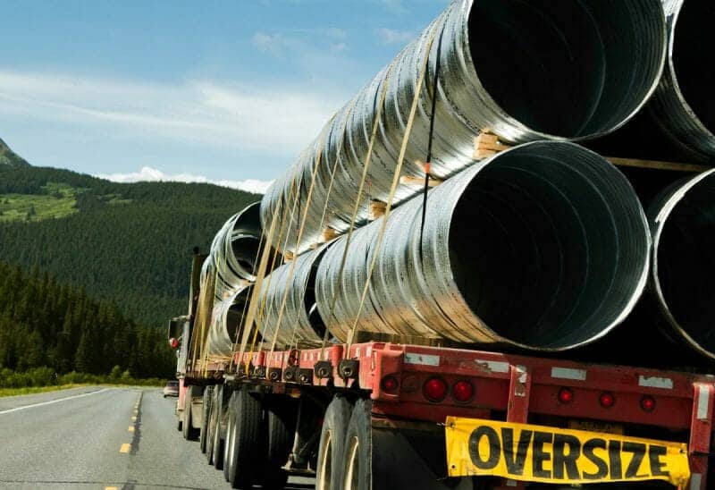 OVERSIZED LOAD OF PIPE ON A FLATBED TRAILER BEHIND A BIG RIG TRUCK