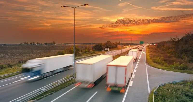 Several Semi trucks on highway at sunrise