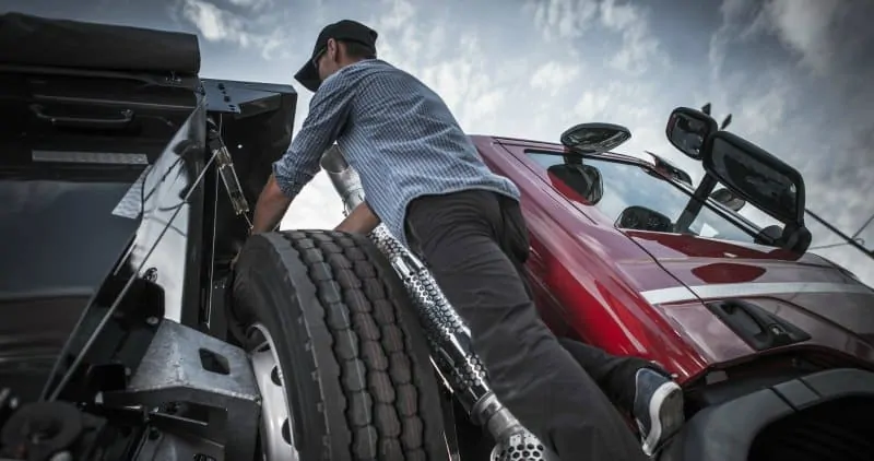 A photo of a man retrieving the spare wheel from a truck. 