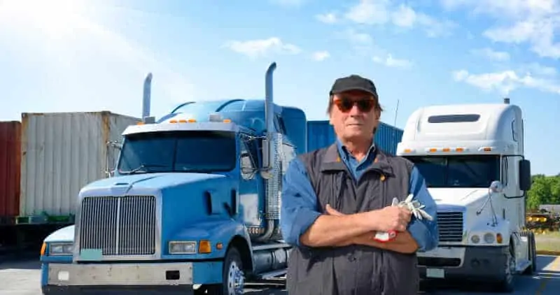 Older truck driver in front of 2 trucks