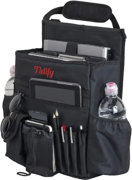 A photo of the Tidify seat organizer. It is full of various objects, like a tablet and water bottle. A handle can be seen at the top for attaching to the back of a seat. 