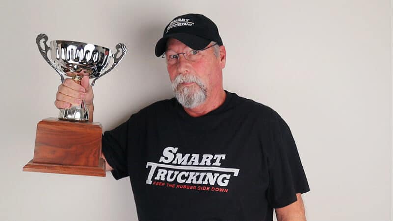 A photo of a man wearing a Smart Trucking t-shirt. He is holding up a large trophy.