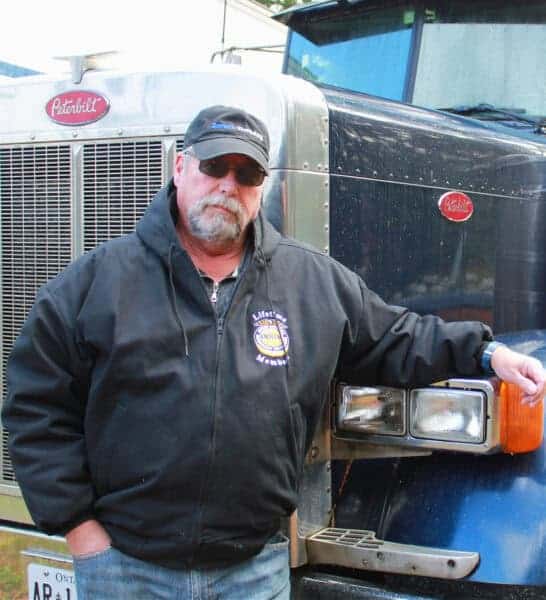 Truck driver standing by a 2004 Peterbilt truck.