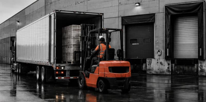 Dock worker loading semi truck and trailer with freight.